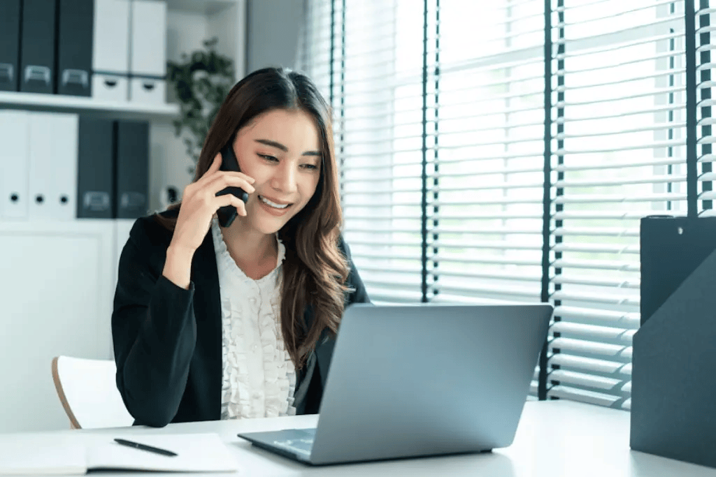 Smiling businesswoman using phone and laptop, representing Mocean SMS messaging campaign for customer service and support.